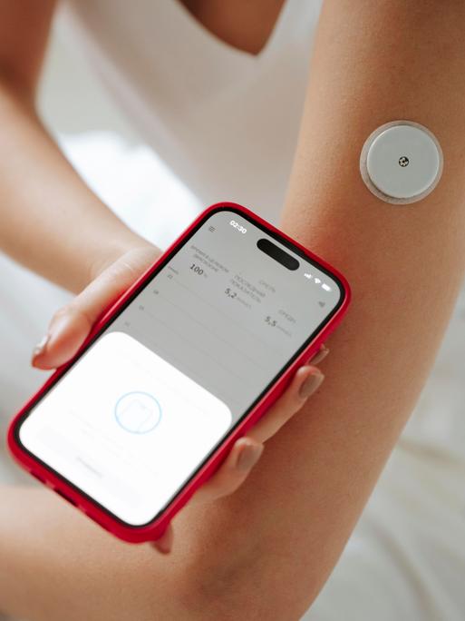 Eine Frau misst mithilfe ihres Smartphones den Blutzucker.