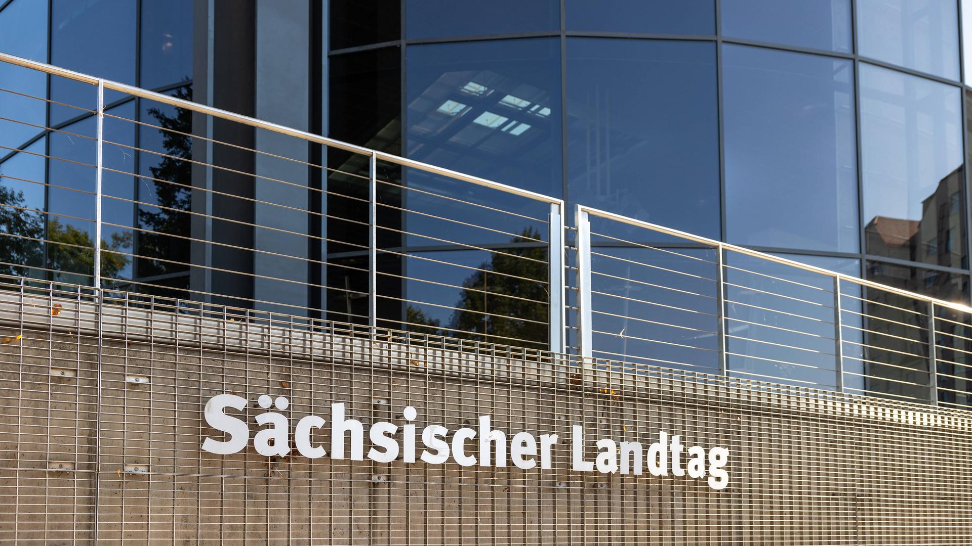 Eine Nahaufnahme des Sächsischen Landtags in Dresden zeigt den Schriftzug Sächsischer Landtag an einer Gitterstruktur vor der modernen Glasfassade des Gebäudes. Eine Nahaufnahme des Sächsischen Landtags in Dresden zeigt den Schriftzug Sächsischer Landtag an einer Gitterstruktur vor der modernen Glasfassade des Gebäudes.