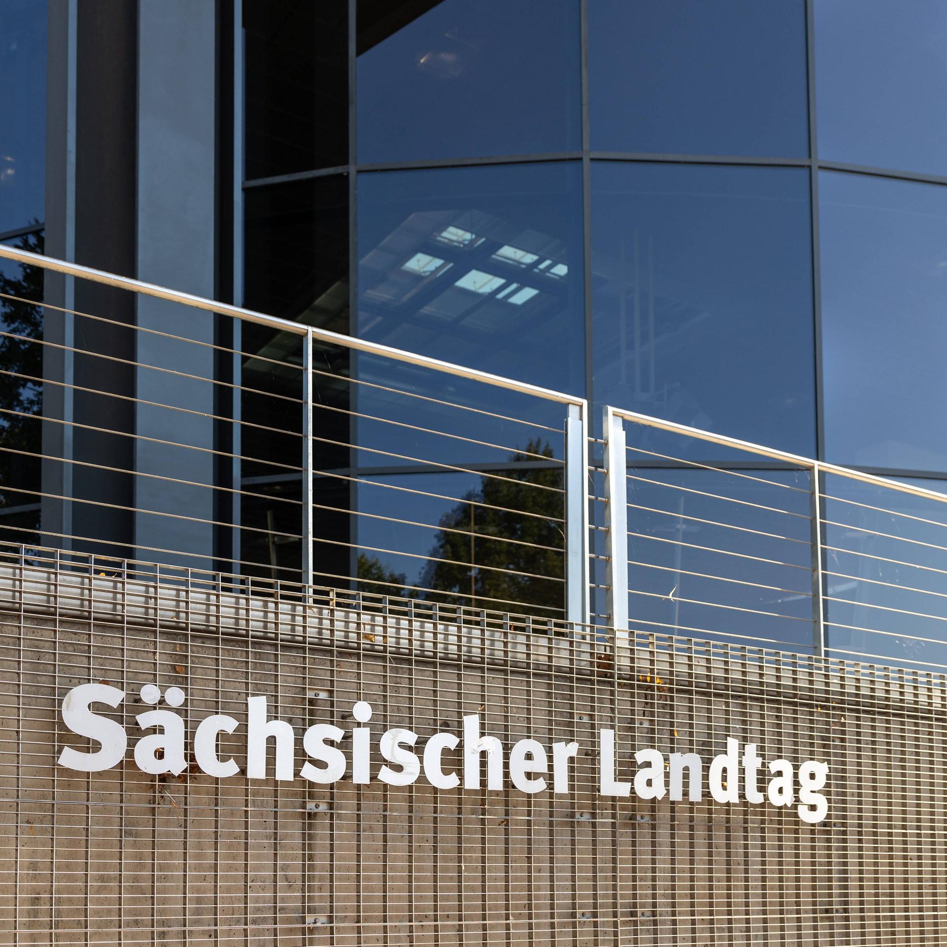 Eine Nahaufnahme des Sächsischen Landtags in Dresden zeigt den Schriftzug Sächsischer Landtag an einer Gitterstruktur vor der modernen Glasfassade des Gebäudes. 