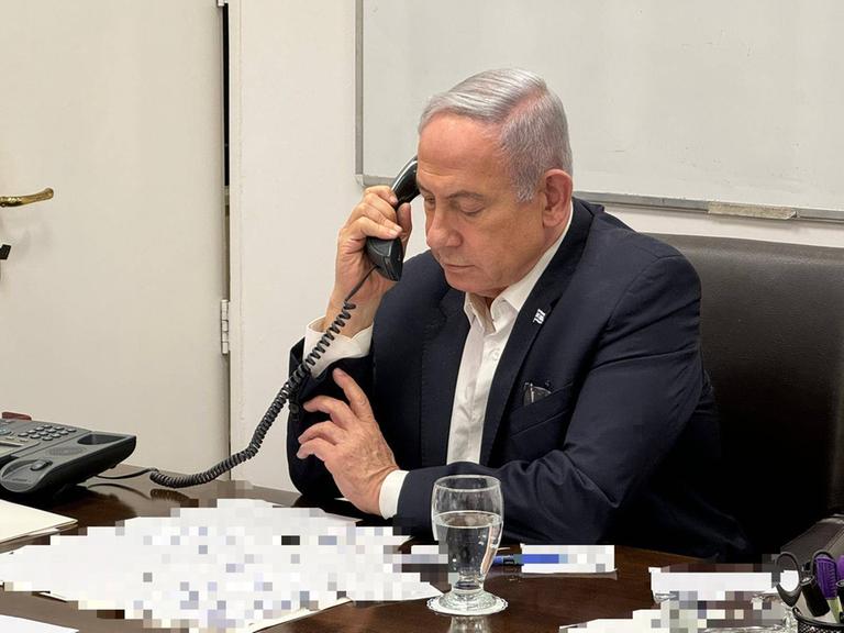 Israels Premier Benjamin Netanjahu am Telefon, verpixelte Dokumente vor sich auf dem Tisch