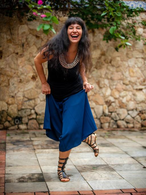 Kateryna Ostrovska in einem blauen Kleid mit Sandalen, lacht in die Kamera.