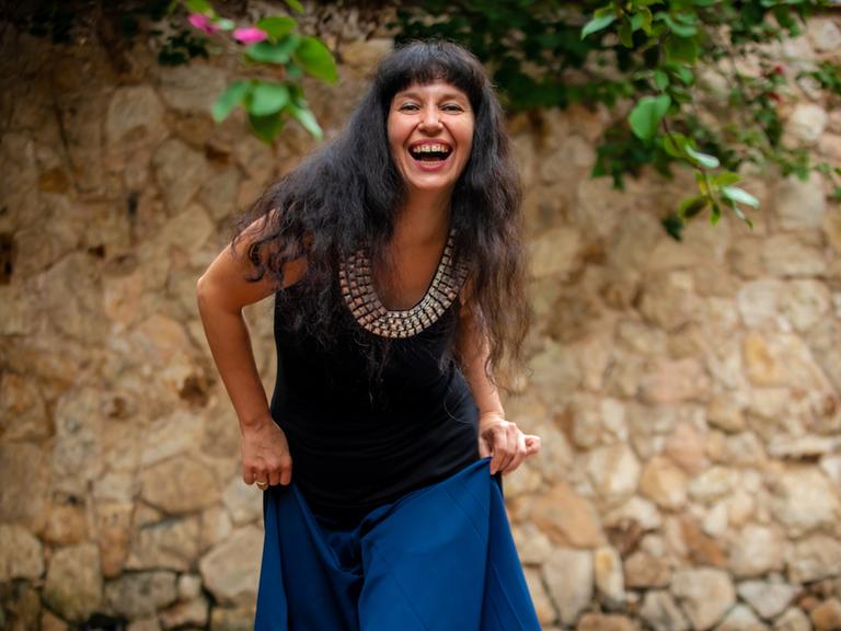 Kateryna Ostrovska in einem blauen Kleid mit Sandalen, lacht in die Kamera.
