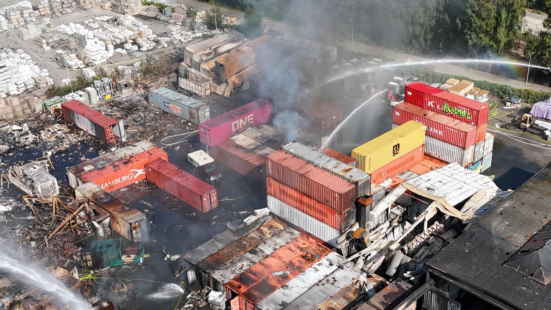 Einsatzkräfte der Feuerwehr löschen einen Brand in einem Industriegebiet im Hamburger Hafen, in dem am Vortag ein Großbrand ausgebrochen war. (Luftaufnahme einer Drohne) 