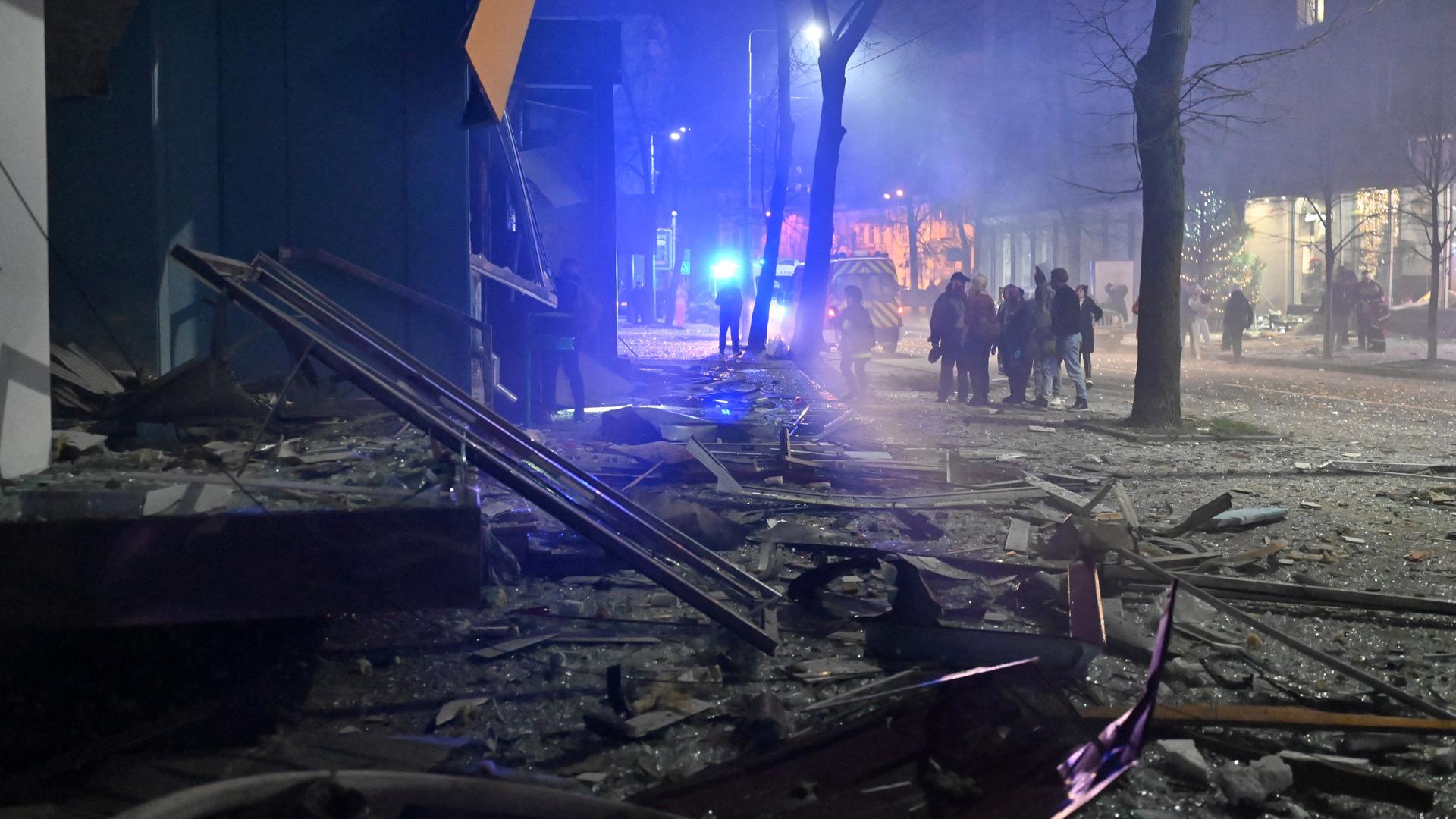 Trümmer liegen auf der Straße, im Hintergrund Menschen und ein Rettungswagen. Trümmer liegen auf der Straße, im Hintergrund Menschen und ein Rettungswagen.