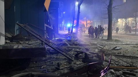 Trümmer liegen auf der Straße, im Hintergrund Menschen und ein Rettungswagen.