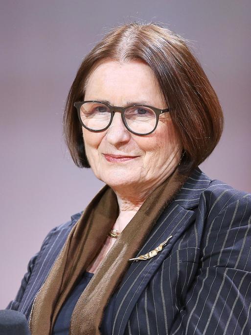 Irina Scherbakowa posiert mit Brille und Nadelstreifen-Blazer auf einem Podium der Frankfurter Buchmesse für ein Pressefoto.