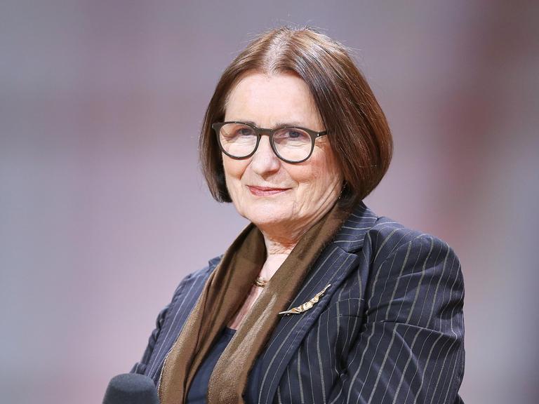 Irina Scherbakowa posiert mit Brille und Nadelstreifen-Blazer auf einem Podium der Frankfurter Buchmesse für ein Pressefoto.