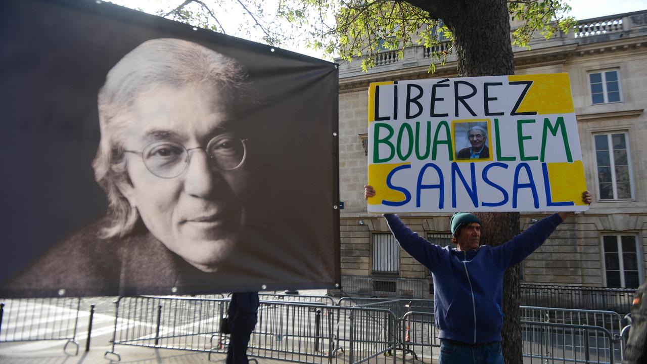 Auf der Straße protestiert ein Mann mit einem Banner für die Freilassung von Boualem Sansal, links daneben ein Plakat, das den franko-algerischen Schriftsteller zeigt.