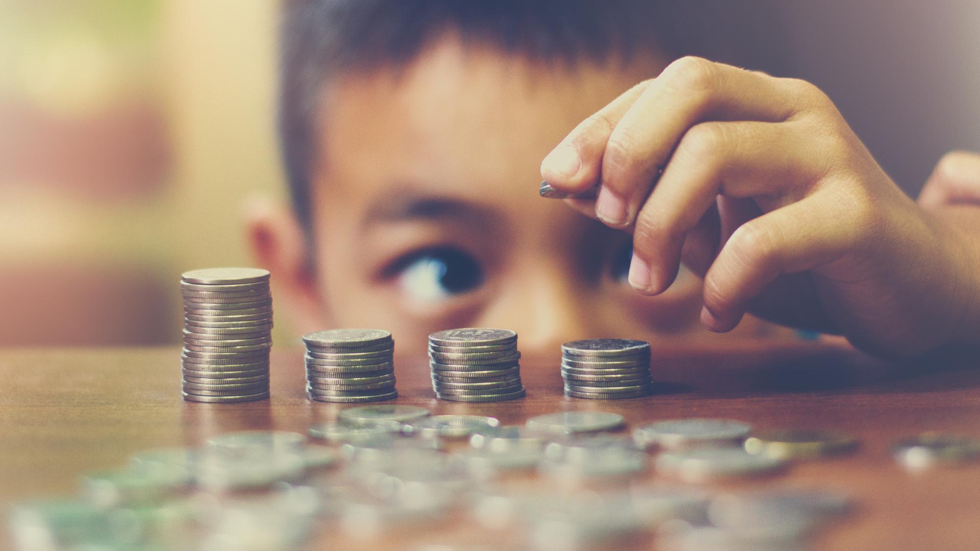 Ein Kind, das gerade eben über die Tischkante schauen kann, stapelt Münzen aufeinander.