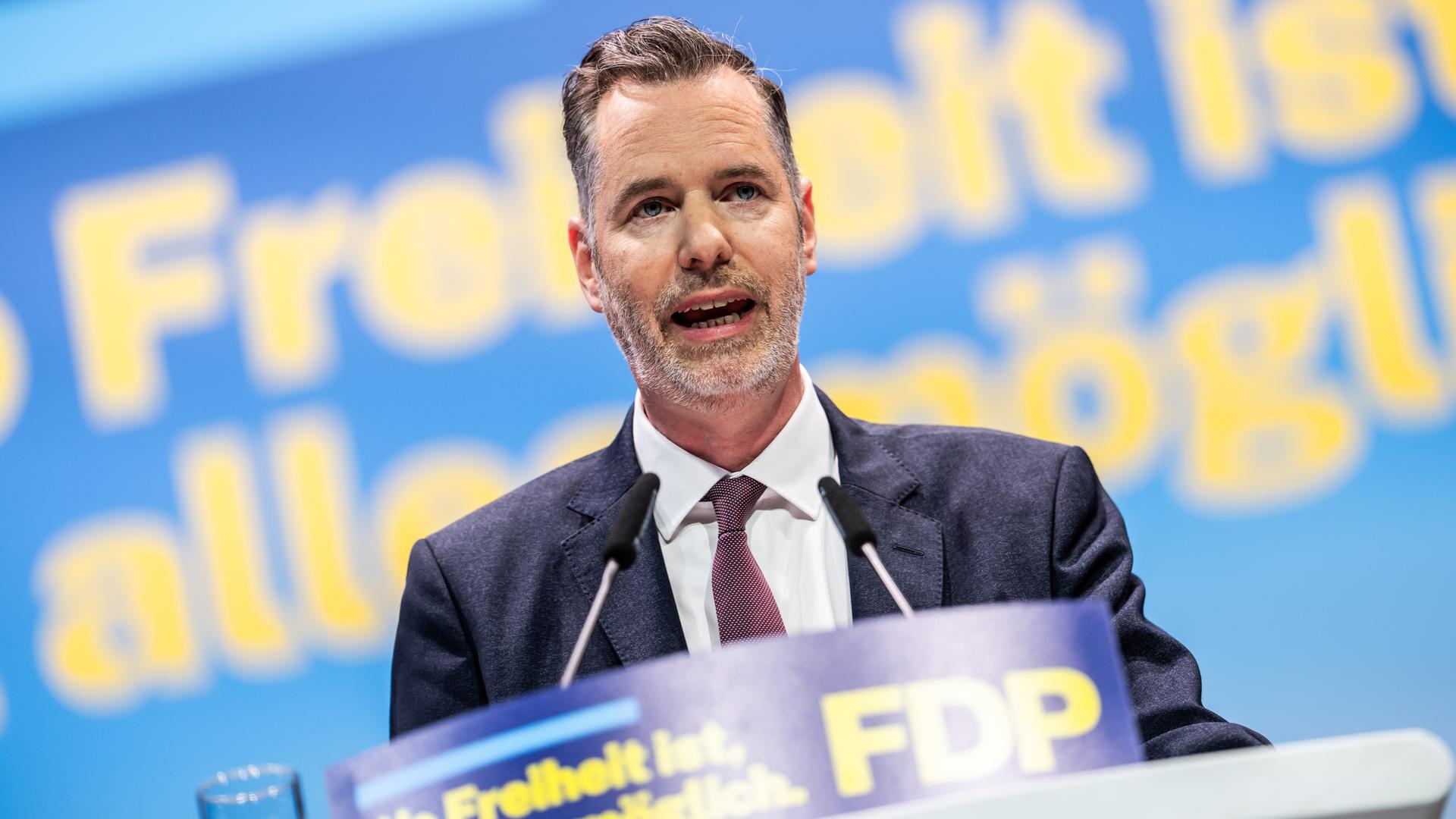 Dürr mit Dreitagebart steht am Rednepuilt und spricht in zwei Mikrofone. Man sieht ihn von vorne. Im Hintergrund unscharf eine Wand mit dem Parteitagsmotto in gelber Schrift.