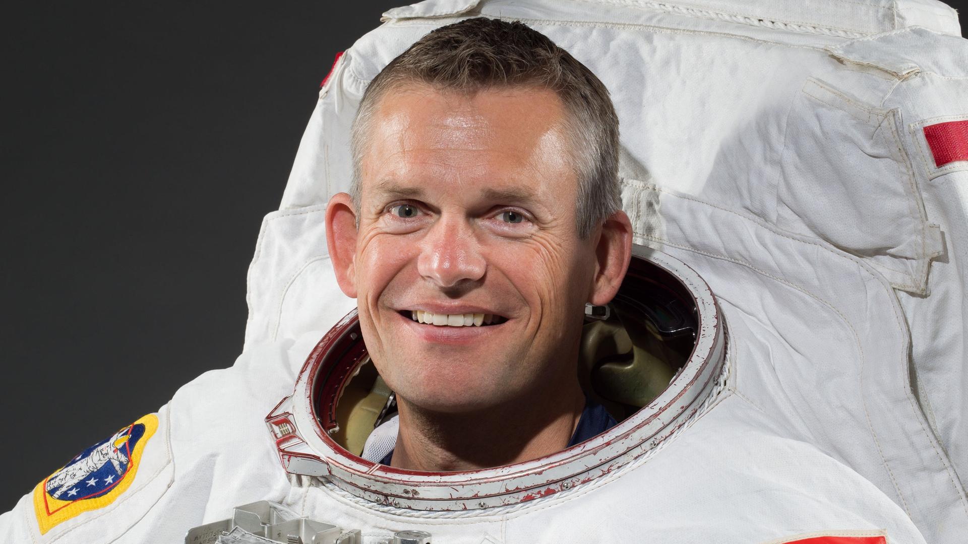 Der ESA-Astronaut Andreas Mogensen trägt einen weißen Raumanzug mit aufgenähter dänischer Flagge und lächelt