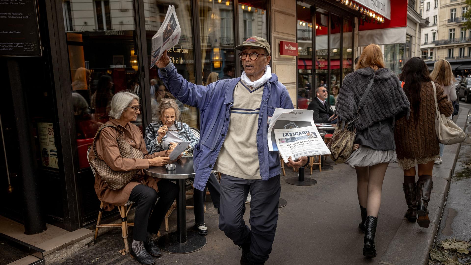 Der Zeitungsverkäufer Ali Akbar läuft durch Paris und bietet seine Ware an Der Zeitungsverkäufer Ali Akbar läuft durch Paris und bietet seine Ware an