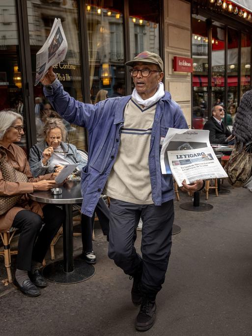 Der Zeitungsverkäufer Ali Akbar läuft durch Paris und bietet seine Ware an