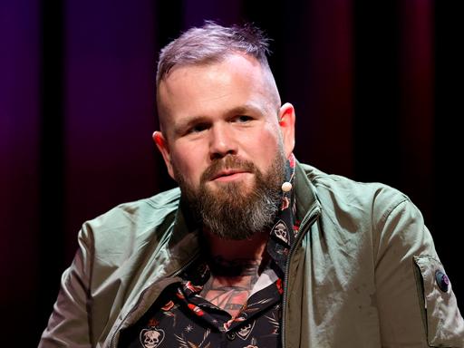 Sänger Jan Gorkow von der Band Feine Sahne Fischfilet sitzt bei einer Veranstaltung im Rahmen der Lit.Cologne 2026 im Theater am Tanzbrunnen vor einem dunklen Hintergrund auf der Bühne. 