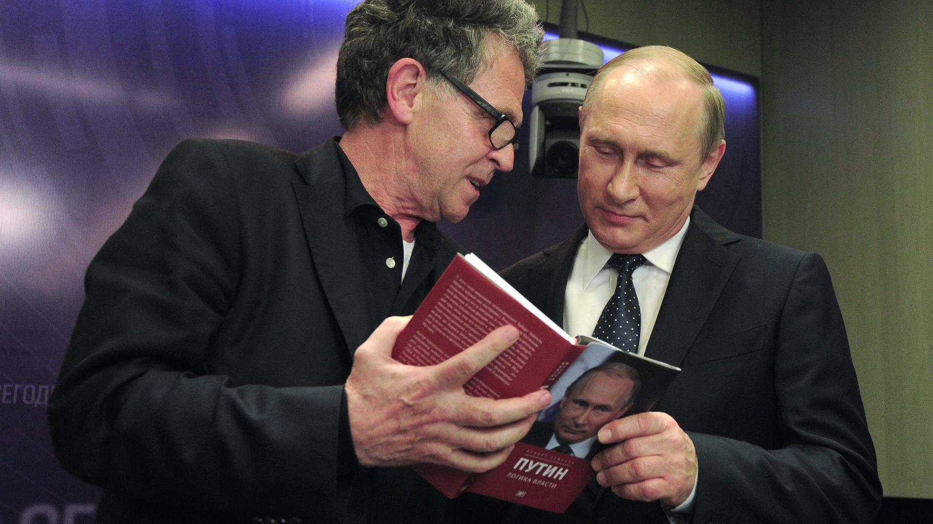 Der deutsche Journalist und Buchautor Hubert Seipel steht neben dem russischen Präsidenten Wladimir Putin. Die beiden schauen in die russische Version von Seibels Buch "Putin: Innenansichten der Macht", dass der Journalist aufgeschlagen in der Hand hält.  