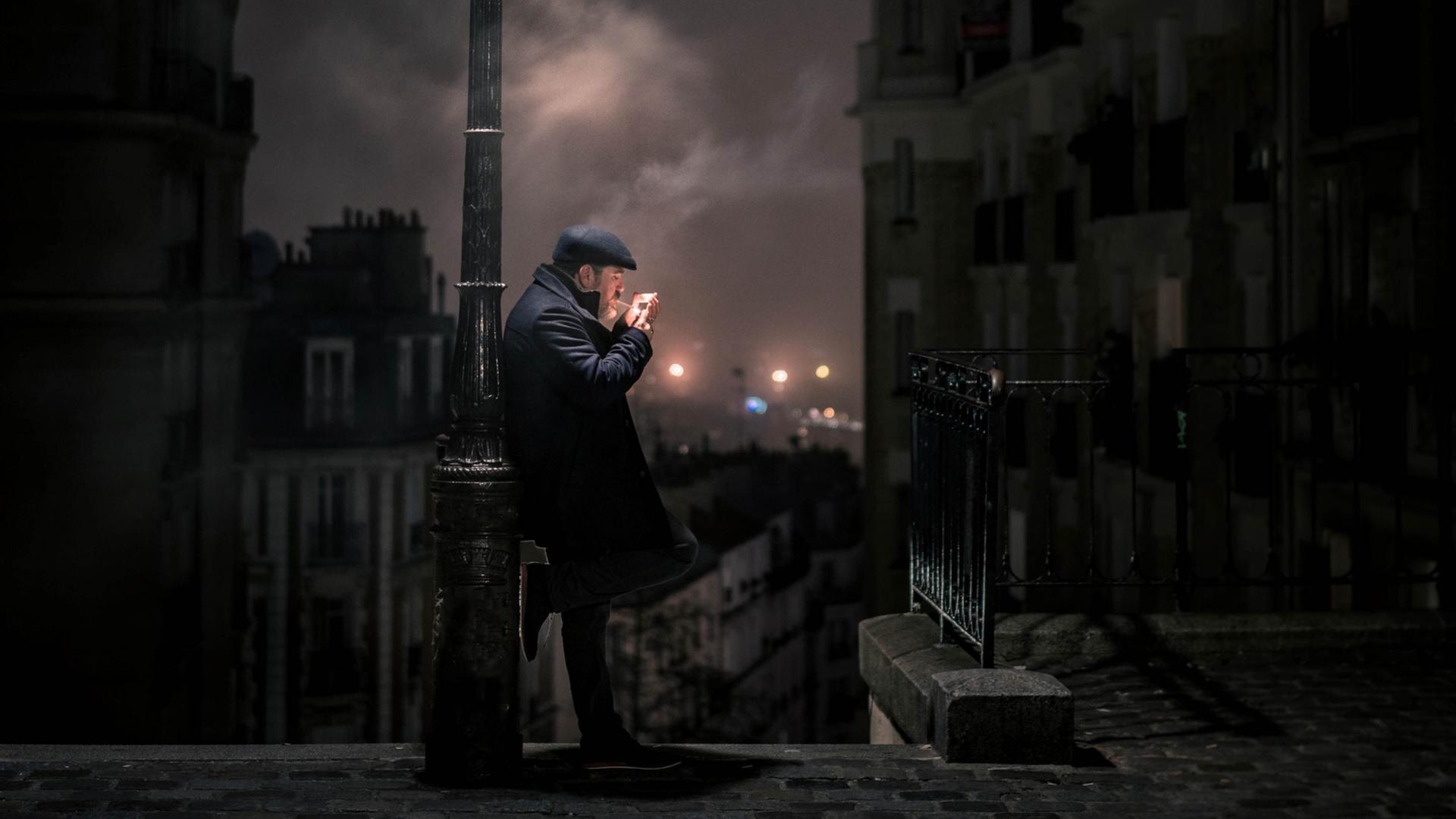 Im nächtlichen Paris lehnt ein Mann an einer Laterne und zündet sich eine Zigarette an. Im nächtlichen Paris lehnt ein Mann an einer Laterne und zündet sich eine Zigarette an.