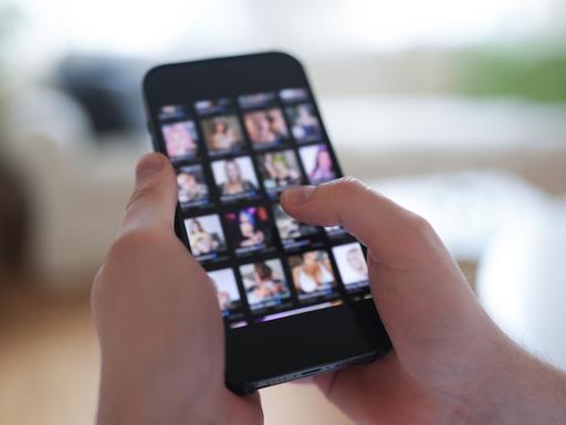 Ein junger Mann schaut sich auf einem Smartphone eine Porno-Internetseite an (gestellte Szene).