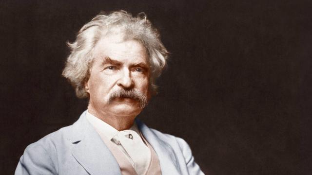 Mark Twain auf einem Foto um 1900. Er sitzt in feinem Zwirn, hat weiße Haare und einen kräftigen Schnauzbart.