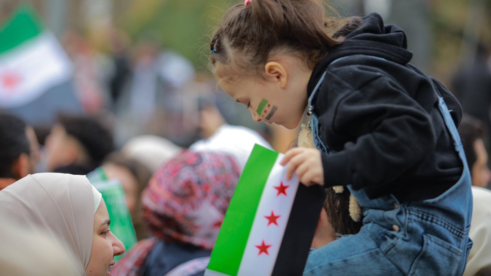 Ein syrisches Mädchen sitzt auf den Schultern einer Person und blickt nach unten