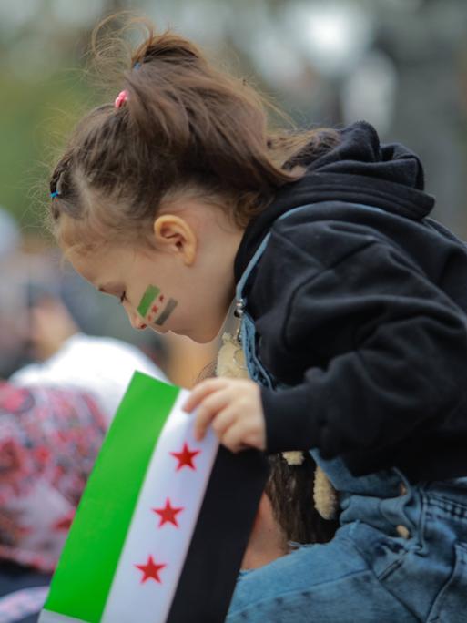 Ein syrisches Mädchen sitzt auf den Schultern einer Person und blickt nach unten