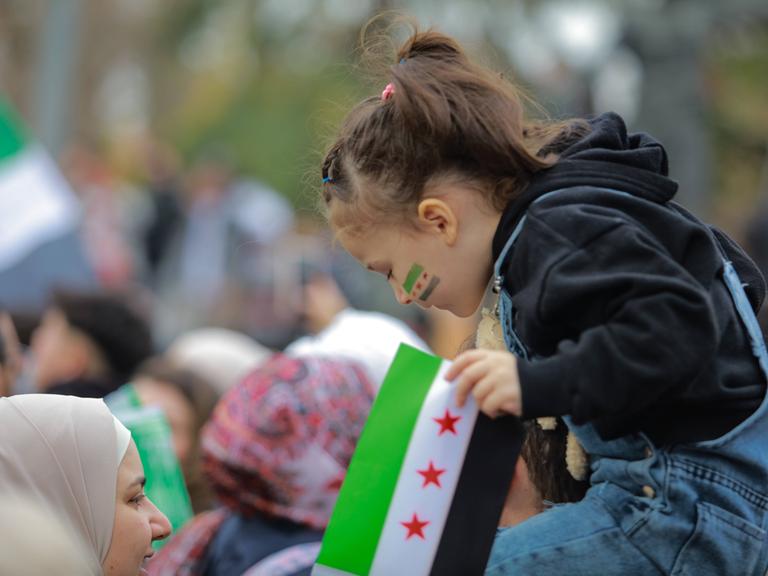 Ein syrisches Mädchen sitzt auf den Schultern einer Person und blickt nach unten