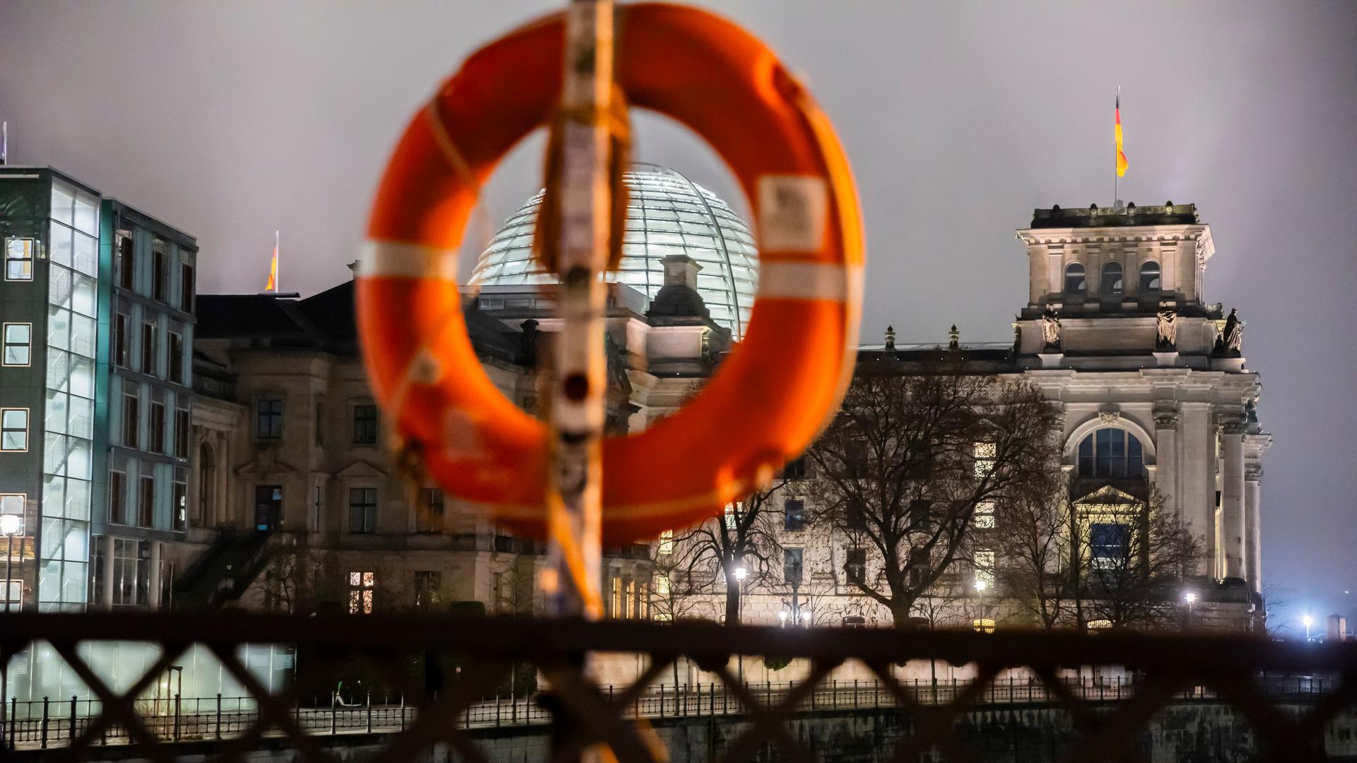 Das Reichstagsgebäude ist am Morgen zu sehen, im Vordergrund sieht man einen Rettungsring, der zur möglichen Rettung von Menschen aus der Spree an einer Brücke hängt. 