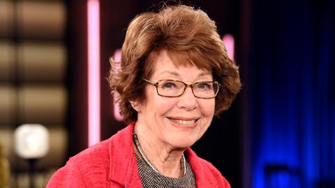 Marianne Koch steht 2025 in einem Fernsehstudio, trägt einen roten Blazer und ein Oberteil in Fischgrätmuster und lächelt. Marianne Koch steht 2025 in einem Fernsehstudio, trägt einen roten Blazer und ein Oberteil in Fischgrätmuster und lächelt.