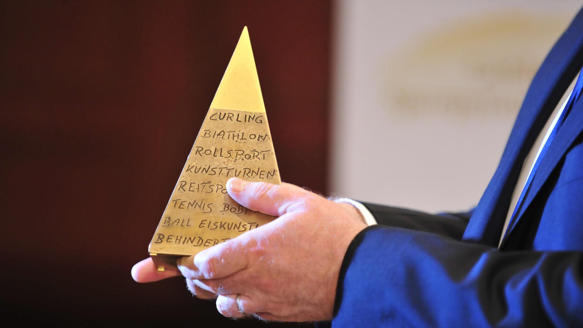 Die Goldene Sportpyramide wird in Händen gehalten. 