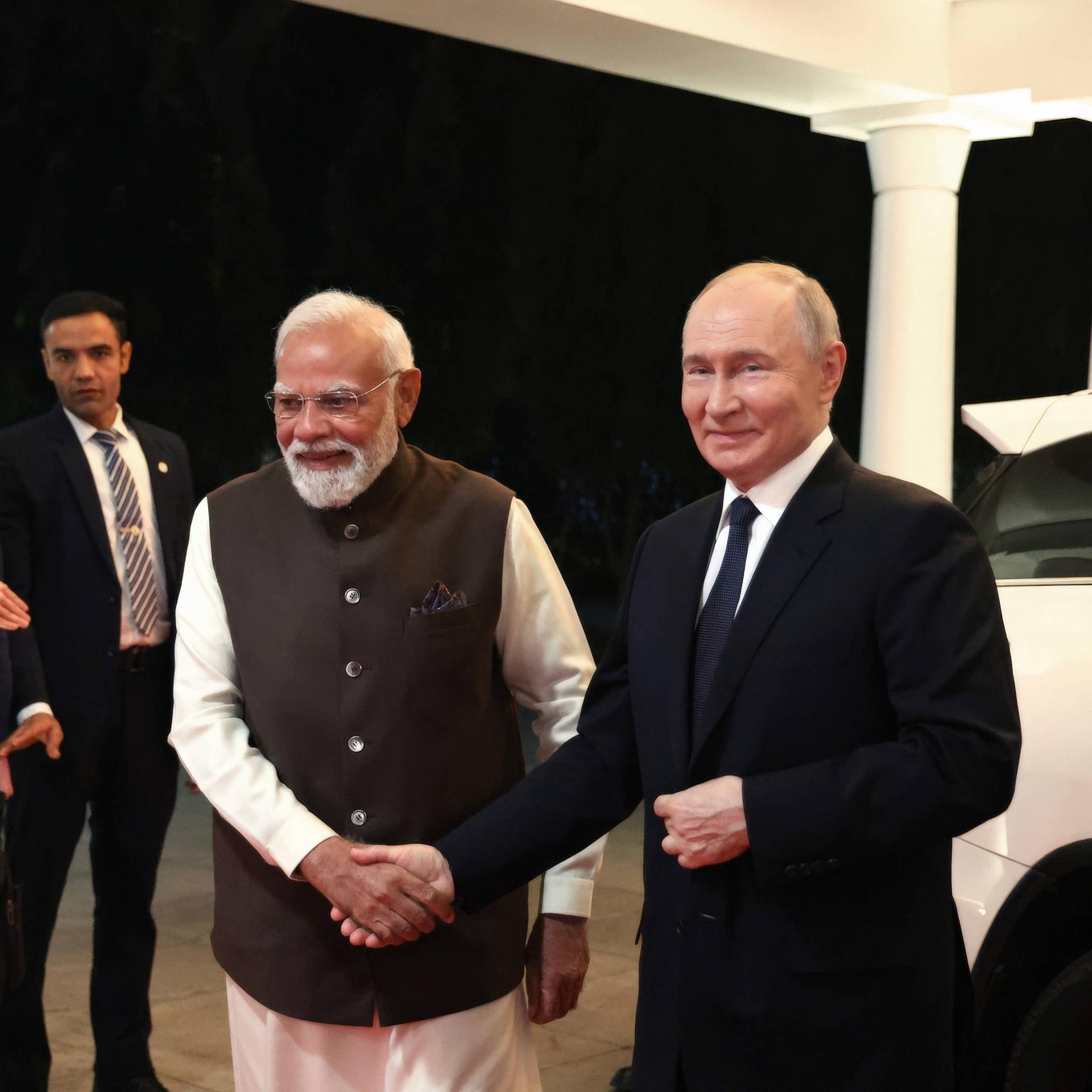 Putin und Modi schütteln sich mit Händeschütteln. Sie stehen nebeneinander und lächeln in Richtung der Kamera. 