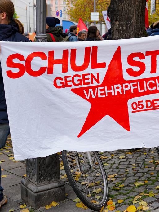 Ein junger Mann hält ein Plakat fest, darauf steht: Schulstreik gegen Wehrpflicht, 5. Dezember, 12 Uhr. Das Foto ist von einer Demo in München, vom 8. November 2025. Ein junger Mann hält ein Plakat fest, darauf steht: Schulstreik gegen Wehrpflicht, 5. Dezember, 12 Uhr. Das Foto ist von einer Demo in München, vom 8. November 2025.