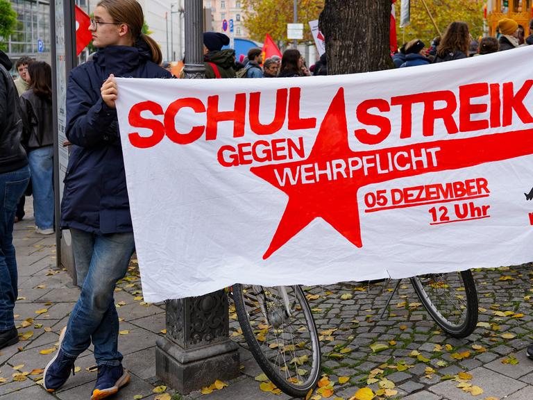 Ein junger Mann hält ein Plakat fest, darauf steht: Schulstreik gegen Wehrpflicht, 5. Dezember, 12 Uhr. Das Foto ist von einer Demo in München, vom 8. November 2025. Ein junger Mann hält ein Plakat fest, darauf steht: Schulstreik gegen Wehrpflicht, 5. Dezember, 12 Uhr. Das Foto ist von einer Demo in München, vom 8. November 2025.