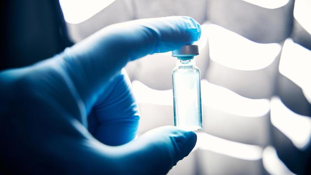 Ein Arzt hält mit Schutzhandschuhen in einem Labor eine Ampulle mit einem Impfstoff (Symbolbild).