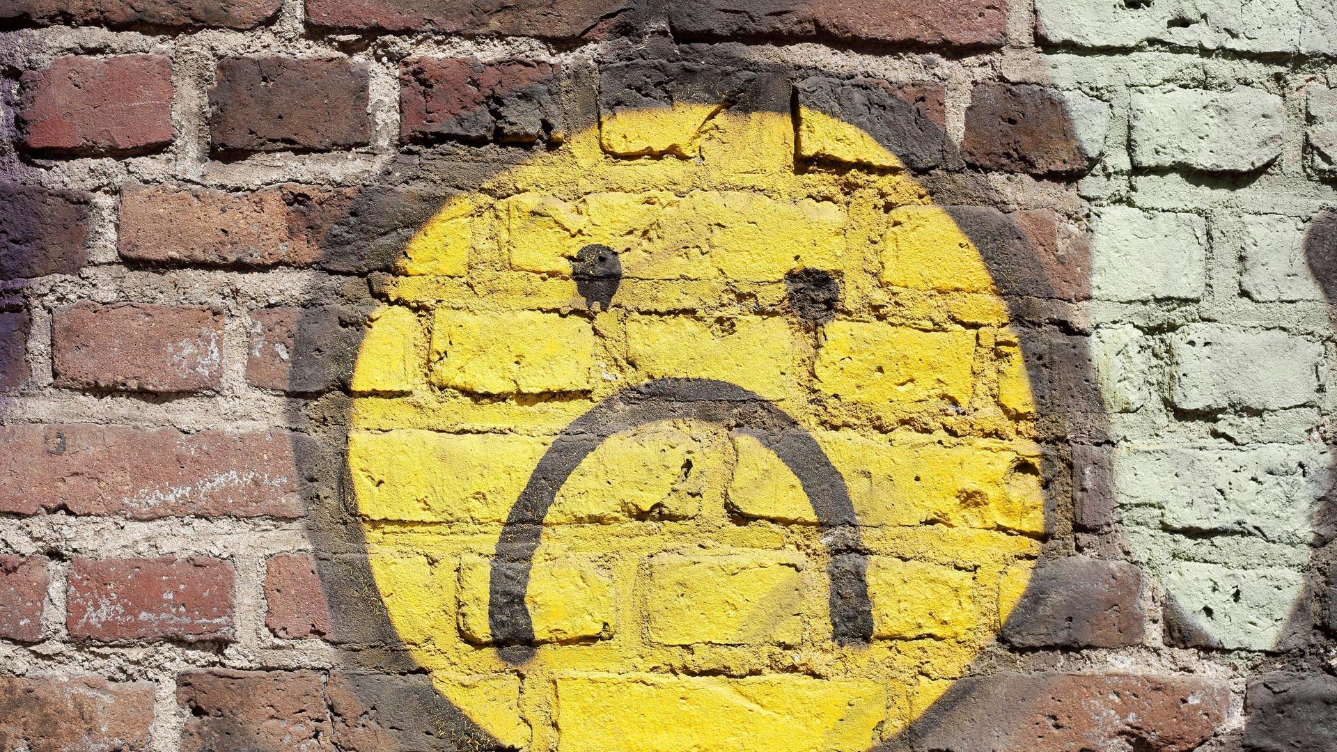 Gelber trauriger Smiley auf eine Backsteinmauer gemal.