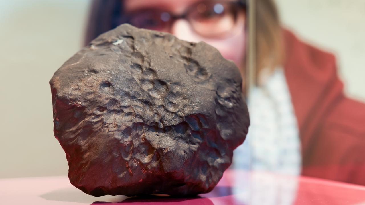 Eine Besucherin betrachtet die strukturierte Oberfläche des Meteorit "Elmshorn" während der Pressekonferenz im Museum der Natur Hamburg.
