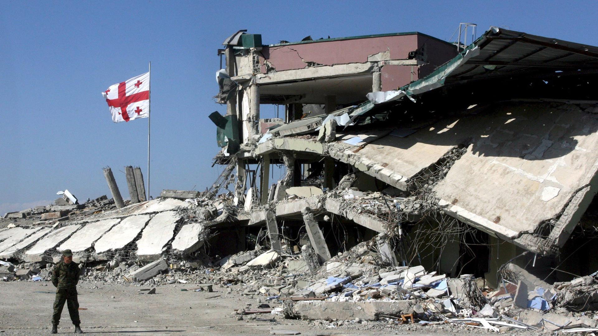 Das Bild zeigt eine zerstörte Militärbasis und eine Flagge von Georgien im Jahr 2008