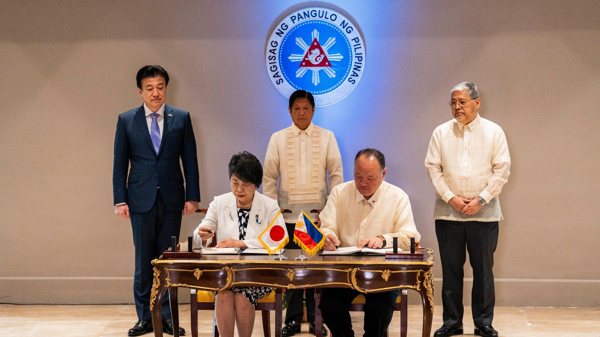 Die japanische Außenministerin Yoko Kamikawa und der philippinische Verteidigungsminister Gilberto Teodoro unterzeichnen einen Vertrag. Hinter ihnen stehen drei Personen. 