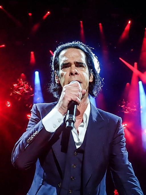 Nick Cave steht im Scheinwerferlicht auf der Bühne und singt frontal in die Kamera