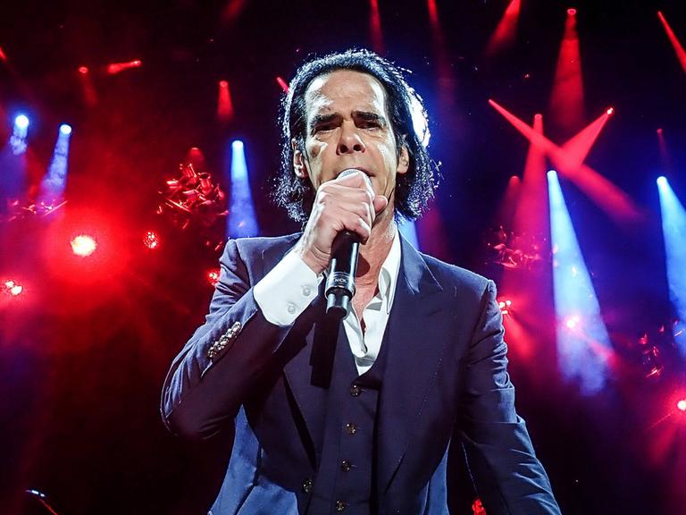 Nick Cave steht im Scheinwerferlicht auf der Bühne und singt frontal in die Kamera