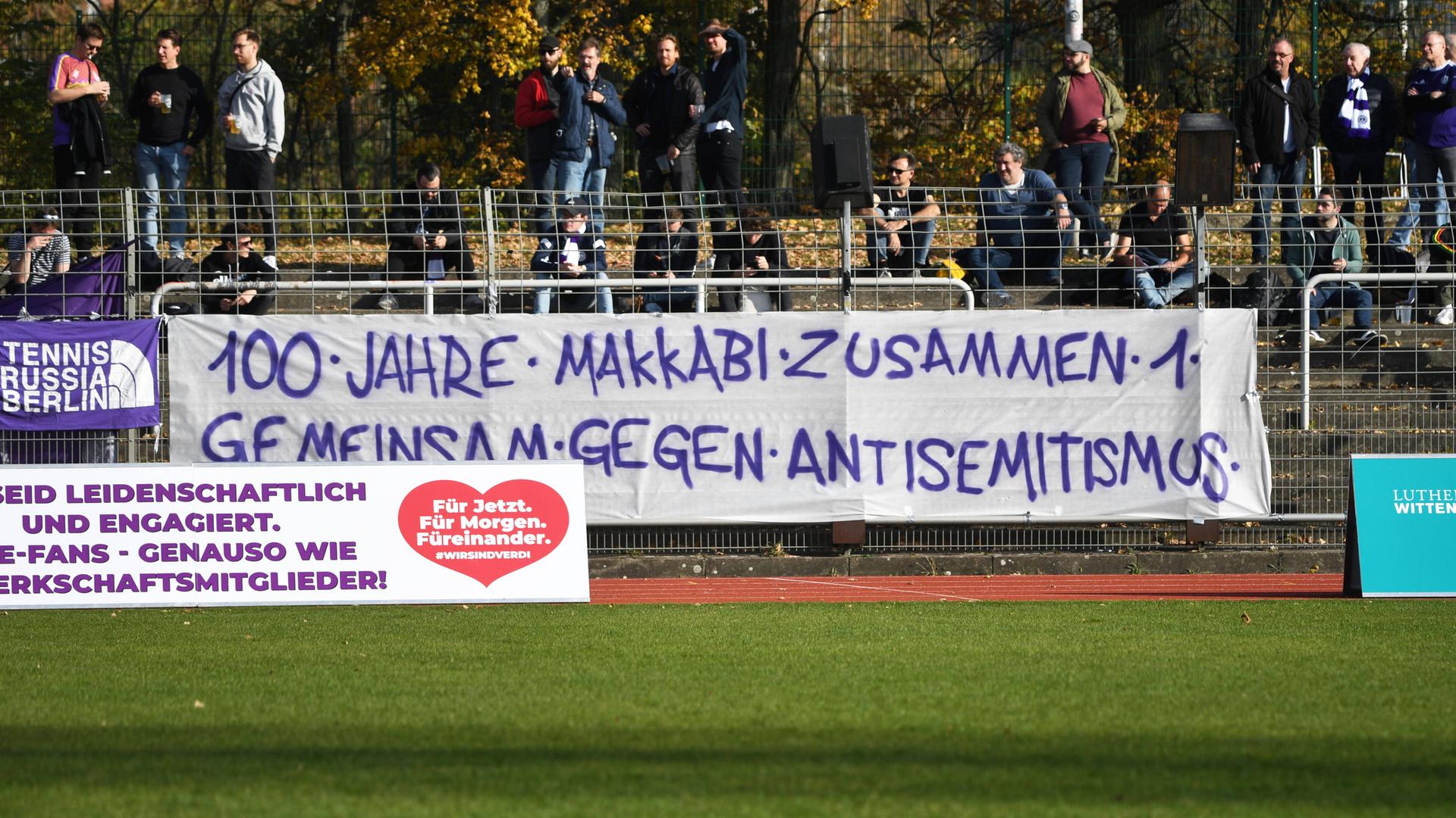 Ein Banner mit der Aufschrift "100 Jahre Makkabi - zusammen - gemeinsam gegen Antisemitismus" hängt in einem Fußballstadion.