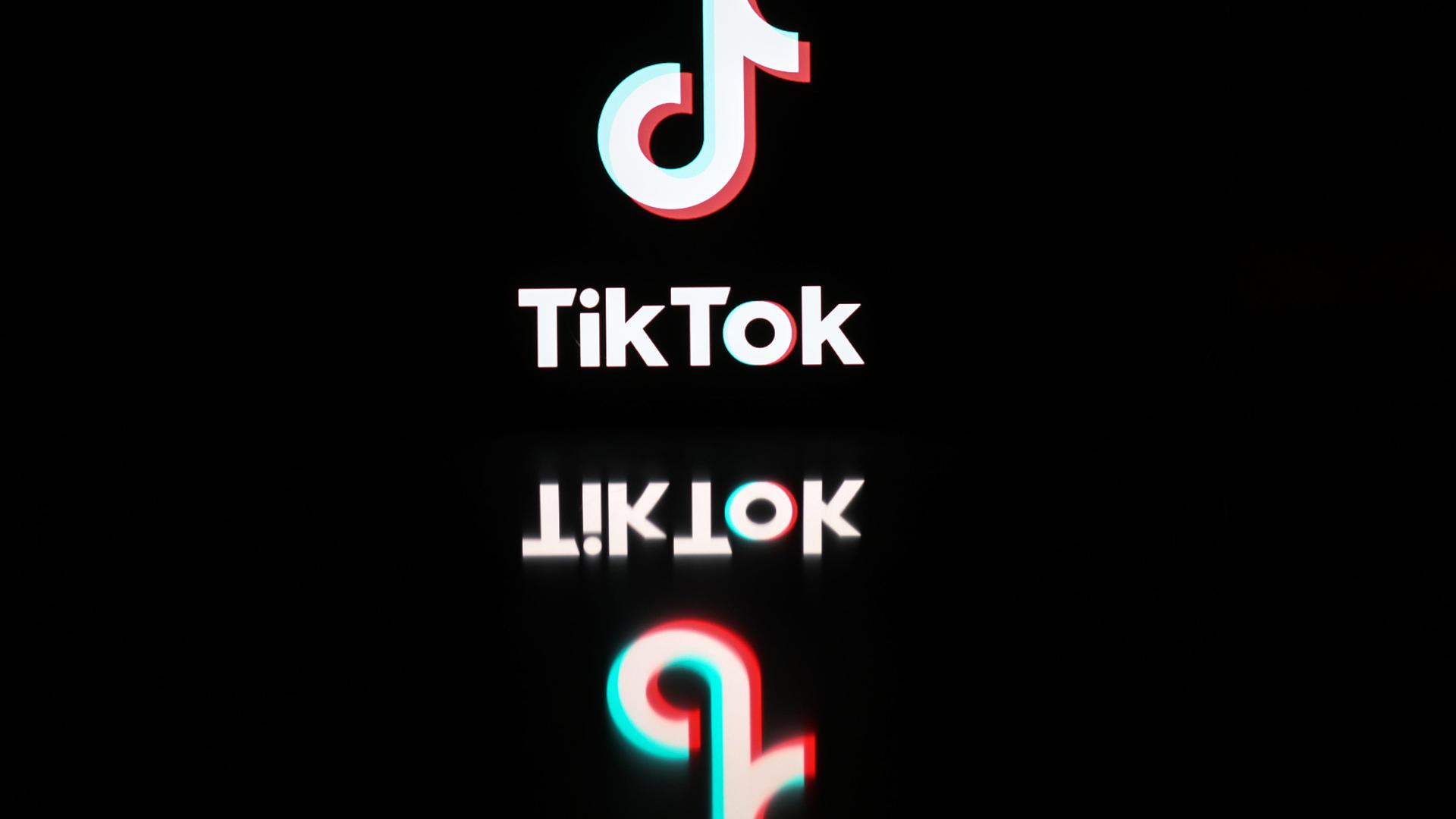 Logo und Schriftzug von TikTok spiegeln sich auf einer schwarzen Oberfläche.