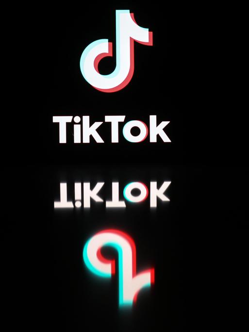 Logo und Schriftzug von TikTok spiegeln sich auf einer schwarzen Oberfläche.