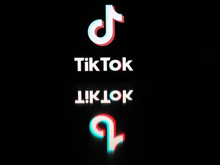 Logo und Schriftzug von TikTok spiegeln sich auf einer schwarzen Oberfläche.