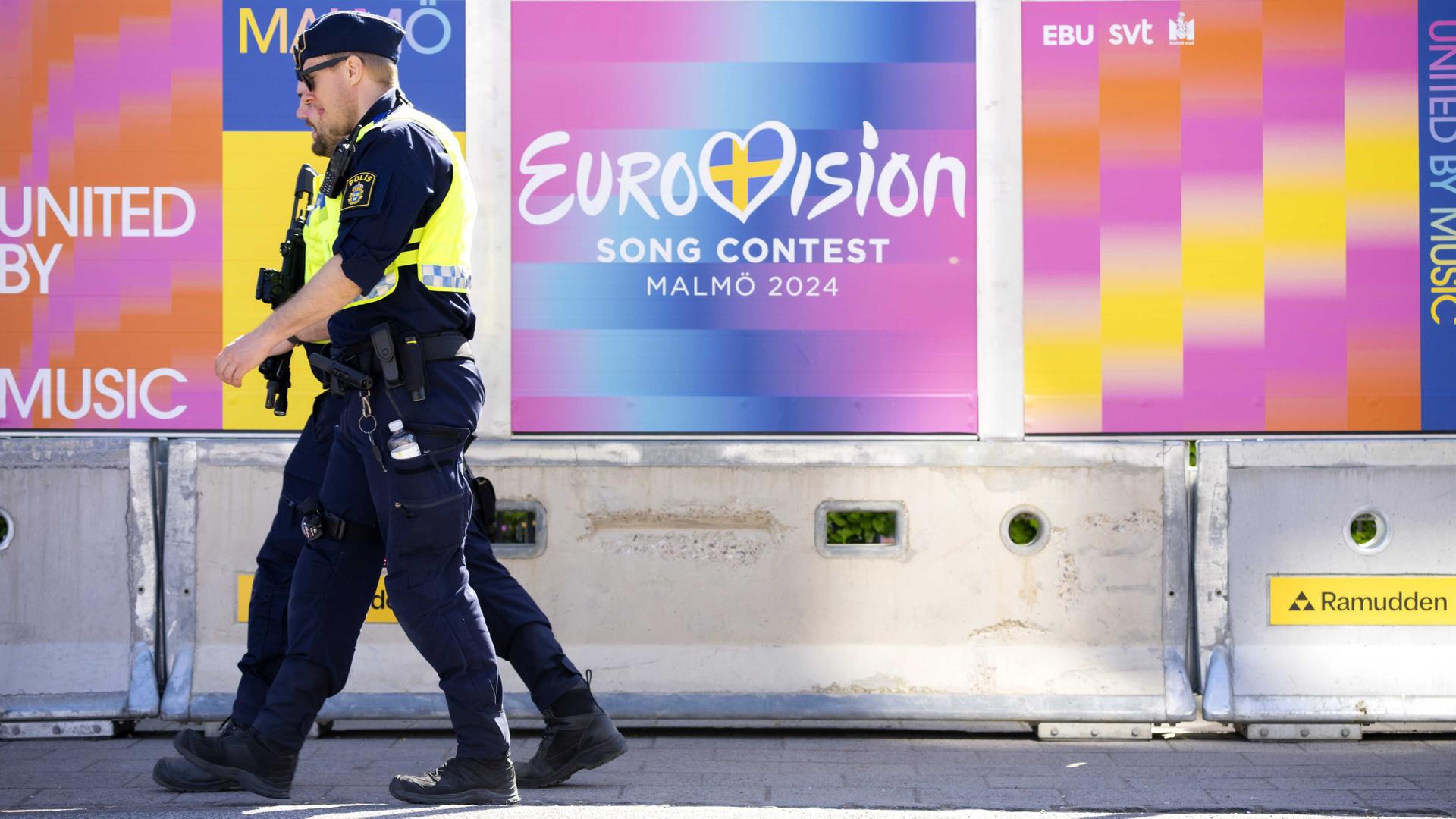 Zwei Polizisten vor einem Zaun in der schwedischen Stadt Malmö, auf dem der ESC-Schriftzug zu sehen ist.