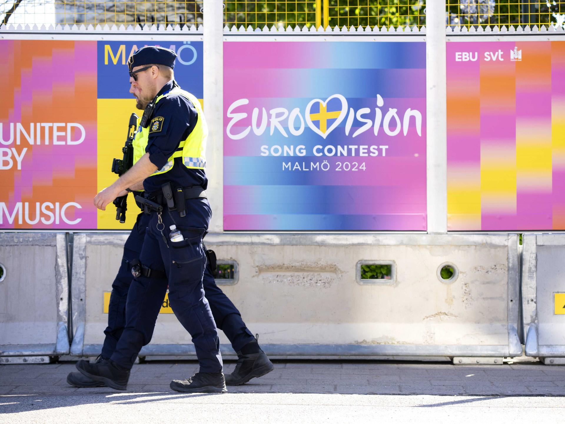 Zwei Polizisten vor einem Zaun in der schwedischen Stadt Malmö, auf dem der ESC-Schriftzug zu sehen ist.
