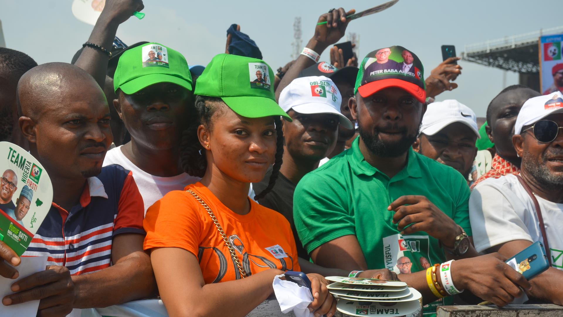 Junge Nigerianerinnen und Nigerianer tragen Caps und Flyer der Partei Labour Party. Sie stehen an einem Wellenbrecher-Zaun und blicken direkt in die Kamera. Junge Nigerianerinnen und Nigerianer tragen Caps und Flyer der Partei Labour Party. Sie stehen an einem Wellenbrecher-Zaun und blicken direkt in die Kamera.