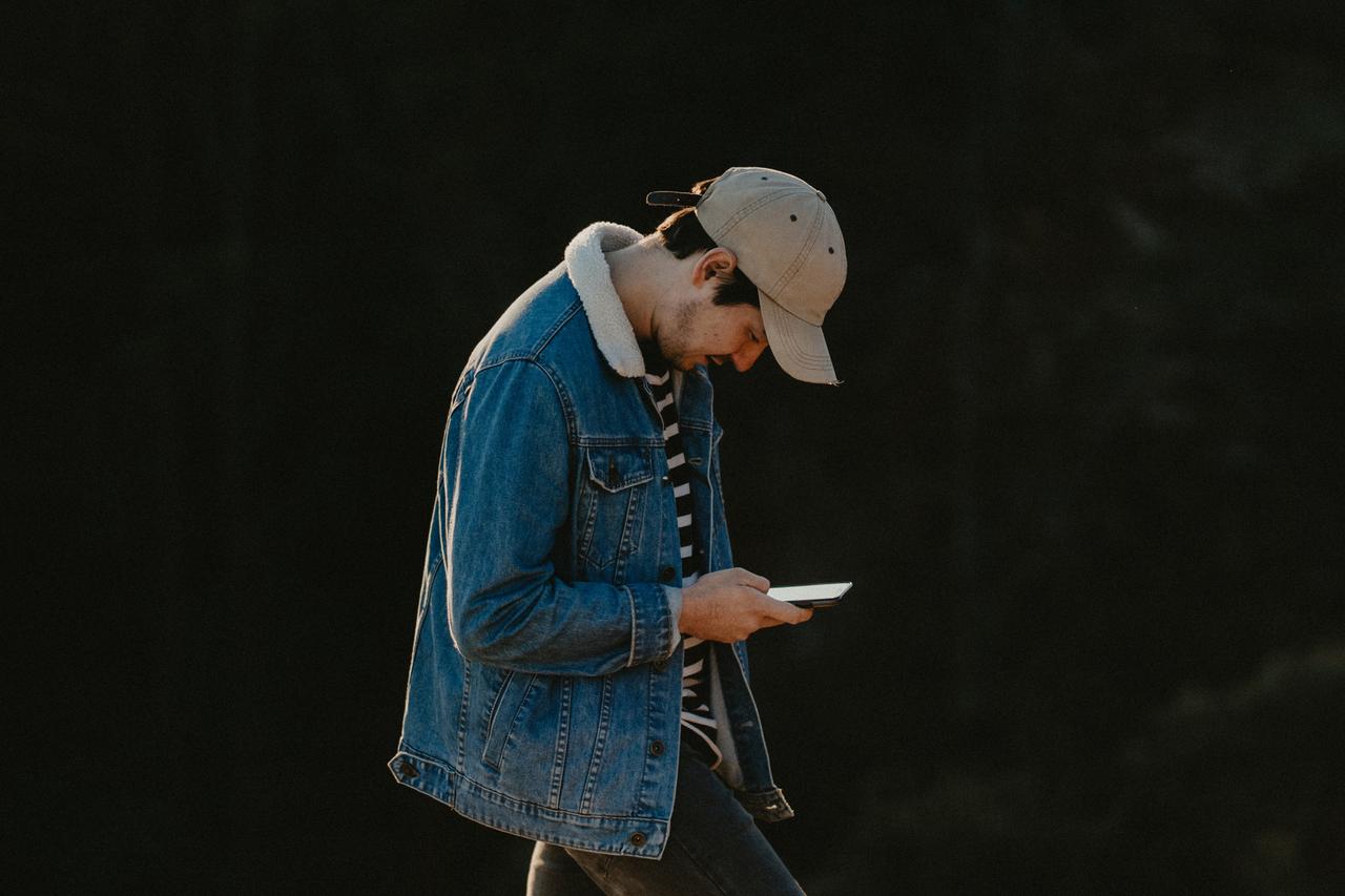 Ein junger Mann mit Käppi schaut im Laufen auf sein Smartphone