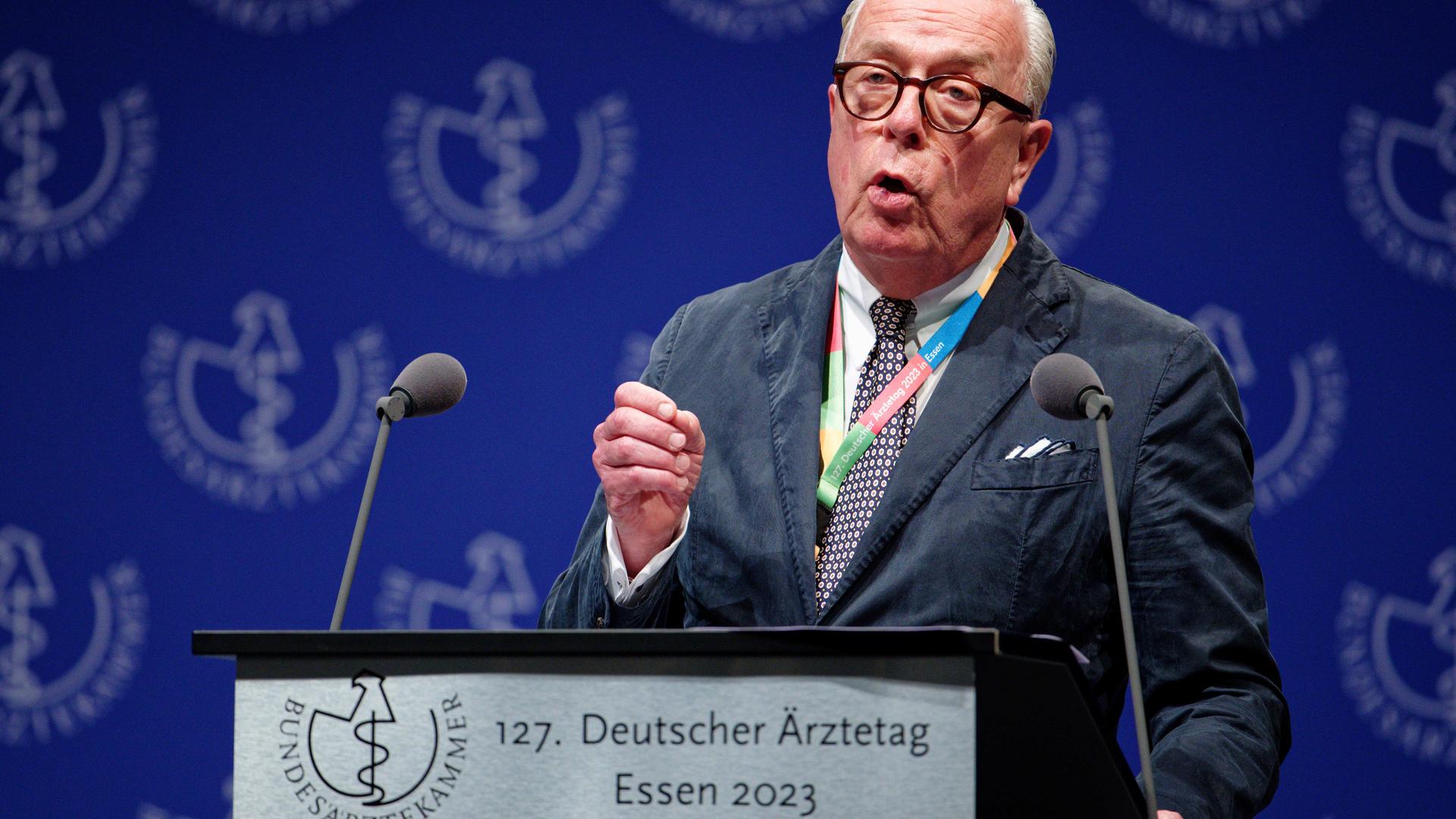 Ärztepräsident Reinhard spricht mit ernster Miene in zwei Mikorofone. Er trägt einen dunklen Anzug. Auf dem Rednerpult ist ein Schild. Auf diesem steht: 127. Deutscher Ärztetag. Essen 2023. Ärztepräsident Reinhard spricht mit ernster Miene in zwei Mikorofone. Er trägt einen dunklen Anzug. Auf dem Rednerpult ist ein Schild. Auf diesem steht: 127. Deutscher Ärztetag. Essen 2023.