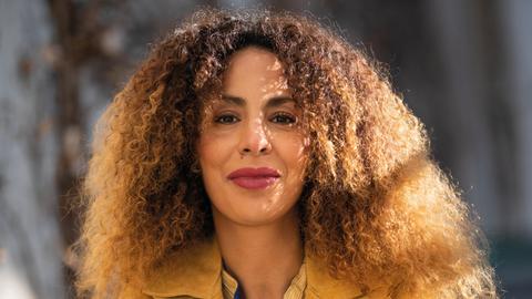 Die Integrationsexpertin Souad Lamroubal hat lange lockige Haare und blickt direkt in die Kamera, der Hintergrund des Fotos ist verschwommen.