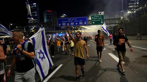 Demontranten laufen in Tel Aviv mit Fahnen auf der Hauptautobahn.