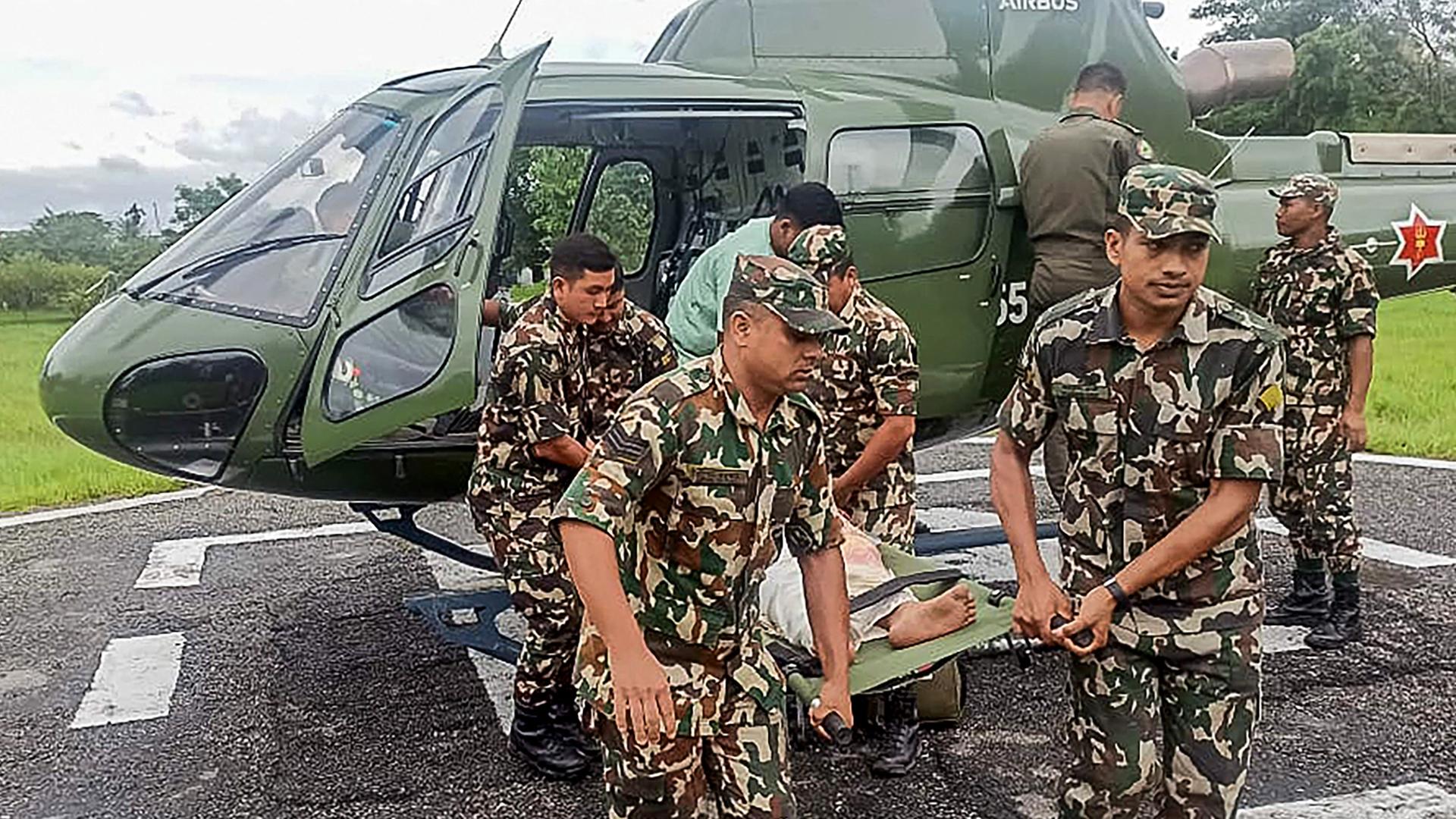 Soldaten aus Nepal tragen eine verletzte Person auf einer Trage aus einem Helikopter heraus